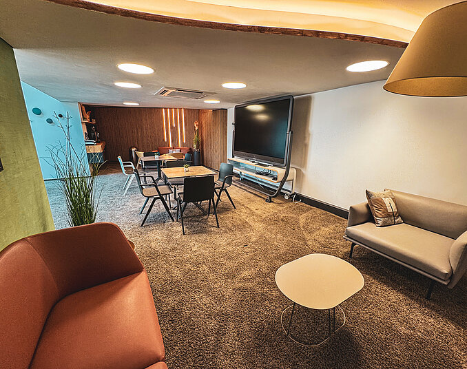 Moderner Tagungsraum mit flexiblem Sitzbereich, großem Präsentationsbildschirm, Sofas und beleuchteter Holzwand