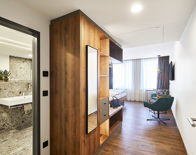 Modernes Hotelzimmer Bodensee mit stilvollem Holzkleiderschrank, gemütlicher Sitzecke und elegantem Badezimmer.
