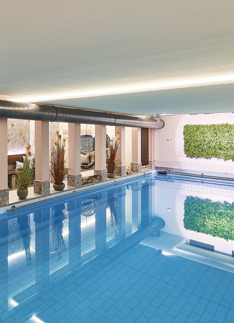 Ein moderner Innenpool mit glattem, blauem Wasser und einem hellen, einladenden Ambiente. An der Wand sind Pflanzen installiert, die zur entspannenden Atmosphäre beitragen. Die Beleuchtung sorgt für eine angenehme Stimmung im Raum.