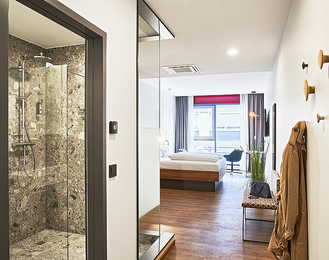Modernes Hotelzimmer mit stilvollem Eingangsbereich, Naturstein-Dusche, gemütlichem Doppelbett und Balkon.