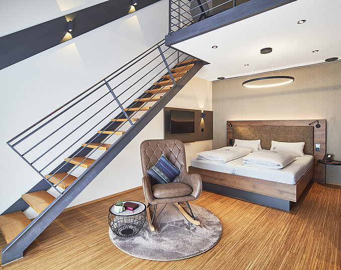 Maisonette-Zimmer mit Doppelbett, Schaukelstuhl und TV – stilvolle Hotelzimmer am Bodensee genießen.