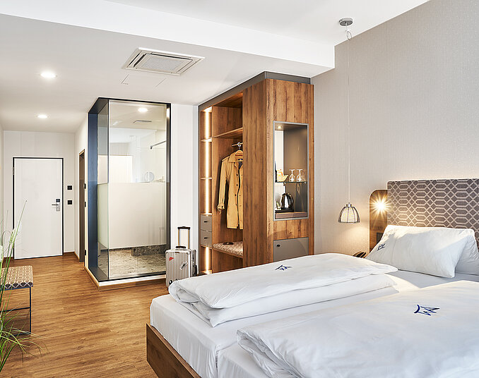 Modernes Hotelzimmer mit gemütlichem Doppelbett, offenem Kleiderschrank und verglastem Badezimmer.