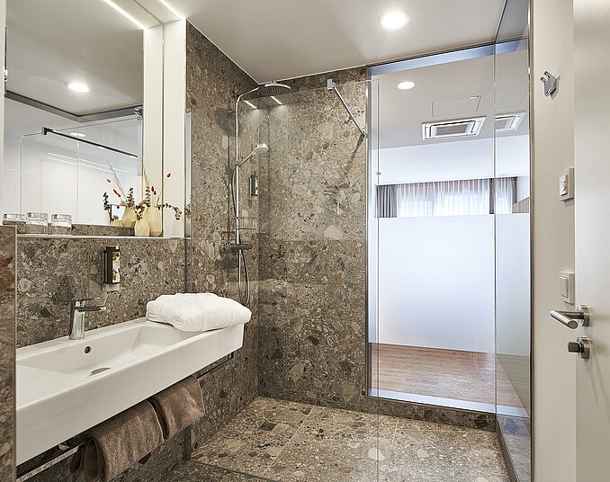 Modernes Hotelbadezimmer mit Natursteinfliesen, begehbarer Regendusche und stilvollem Waschbecken.